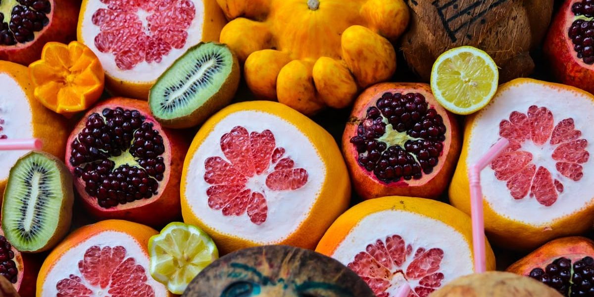 Colorful display of various fruits including grapefruit, pomegranate, coconuts, and citrus in a vibrant market setting.